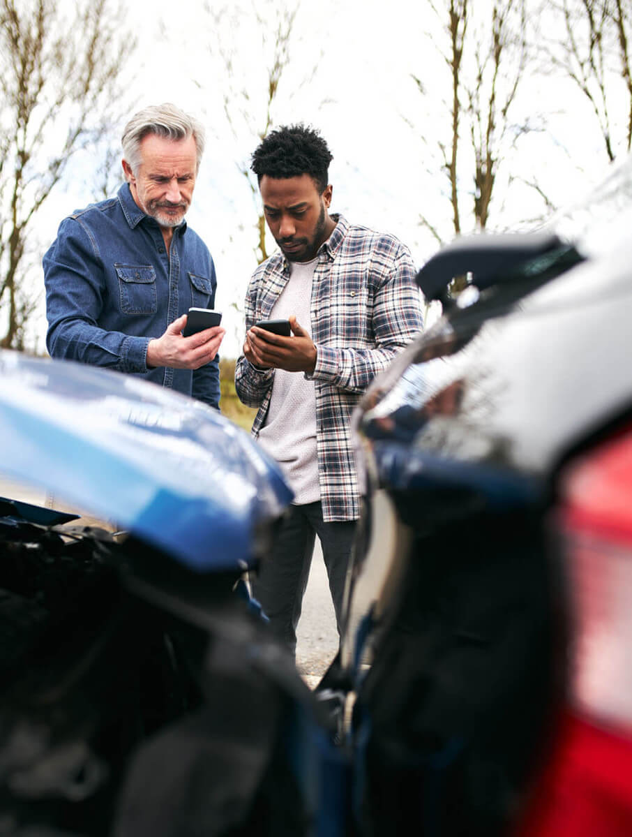 Two men standing outside their cars looking at phones after a car accident